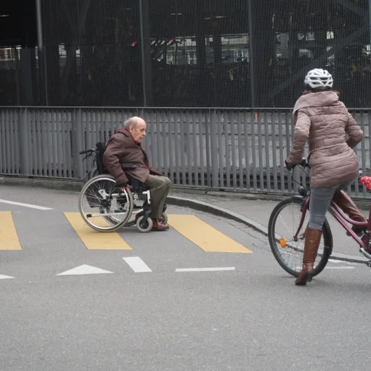 Rollstuhlfahrer überquert Strasse vor Velofahrerin