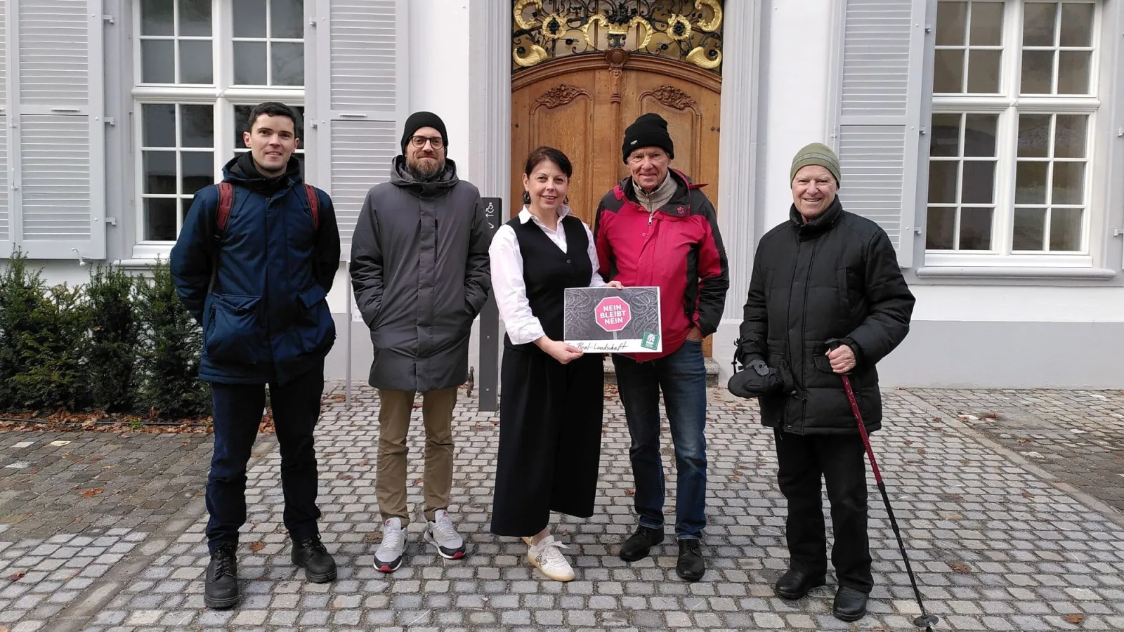 Vier Männer und eine Frau stehen in einer Reihe. Einer übergibt der Landschreiberin einen Umschlag mit den Petitionsunterschriften. Im Hintergrund ist das Regierungsgebäude in Liestal zu sehen.