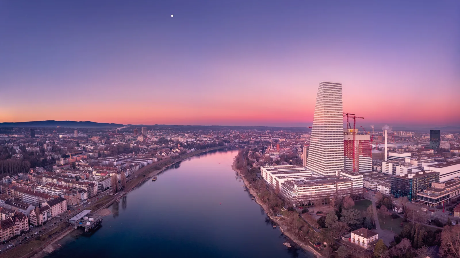 Panoramablick auf Basel nach Sonnenuntergang. Im Vordergrund sind der Rhein und die Roche-Türme zu sehen.