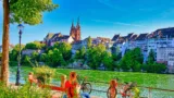 Sehr farbiges Foto des Basler Münsters, davor der Rhein und mehrere am Geländer abgestellte Velos.